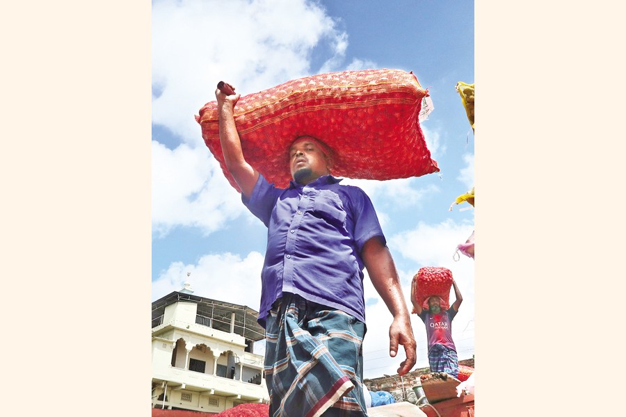 A labourer was photographed carrying a sack of onion in the city's wholesale kitchen market Shyambazar on Friday. Price of the key cooking ingredient jumped by Tk 40 to Tk 120 per kg in a span of just one week. — FE Photo
