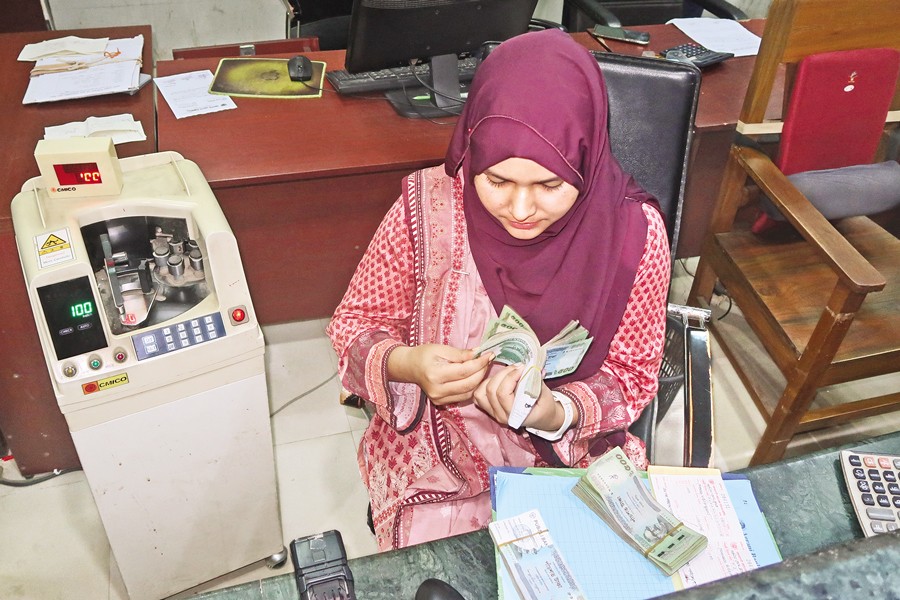 A staffer is counting notes at a bank counter in Dhaka.