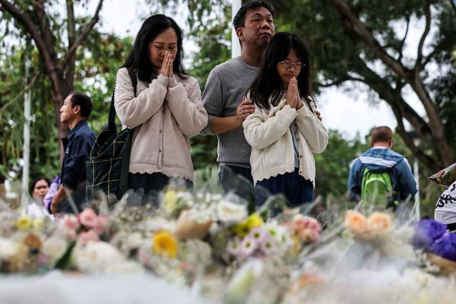 People pray as they come to lay flowers at the makeshift memorial to the victims of the Wang Fuk Court housing complex's deadly fire, in Tai Po, Hong Kong, China, November 30, 2025.