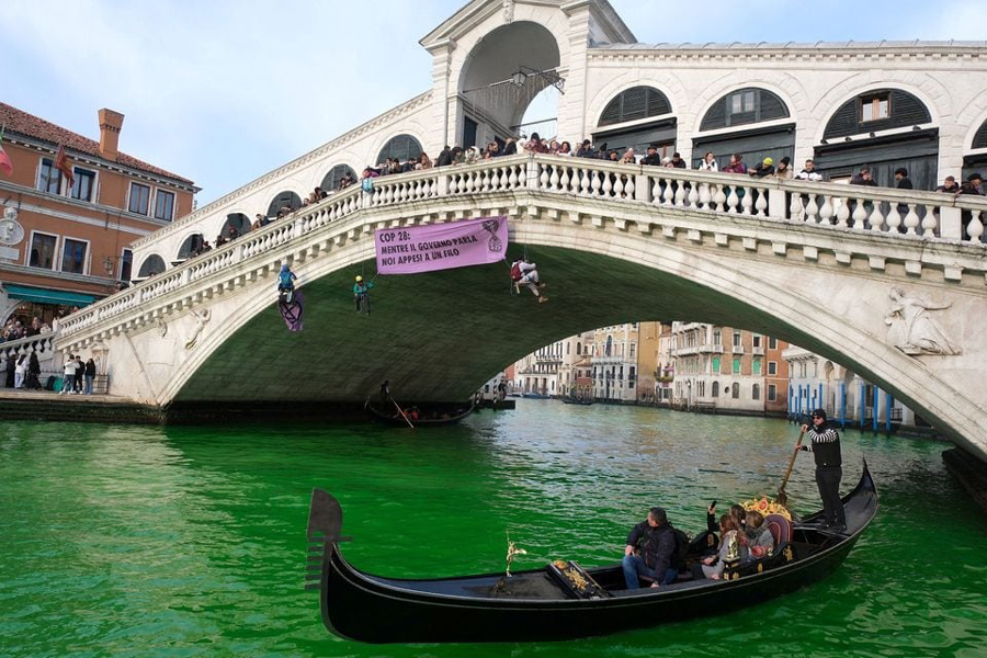 People ride in boats as waters of Grand Canal turned green after a protest by 'Extinction Rebellion' climate activists in Venice, Italy, December 9, 2023.