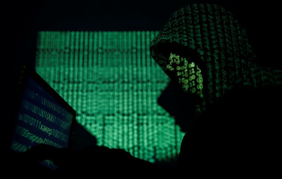 A hooded man holds a laptop computer as cyber code is projected on him in this illustration picture taken on May 13, 2017. REUTERS/Kacper Pempel/Illustration/File Photo