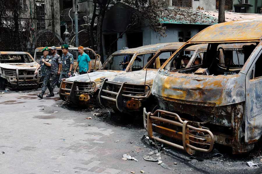 Security personnel walking past damaged vehicles of a government-owned organisation, that were set afire by a mob during clashes after violence erupted following protests by students against government job quotas, in Dhaka on July 22, 2024 –Reuters file photo