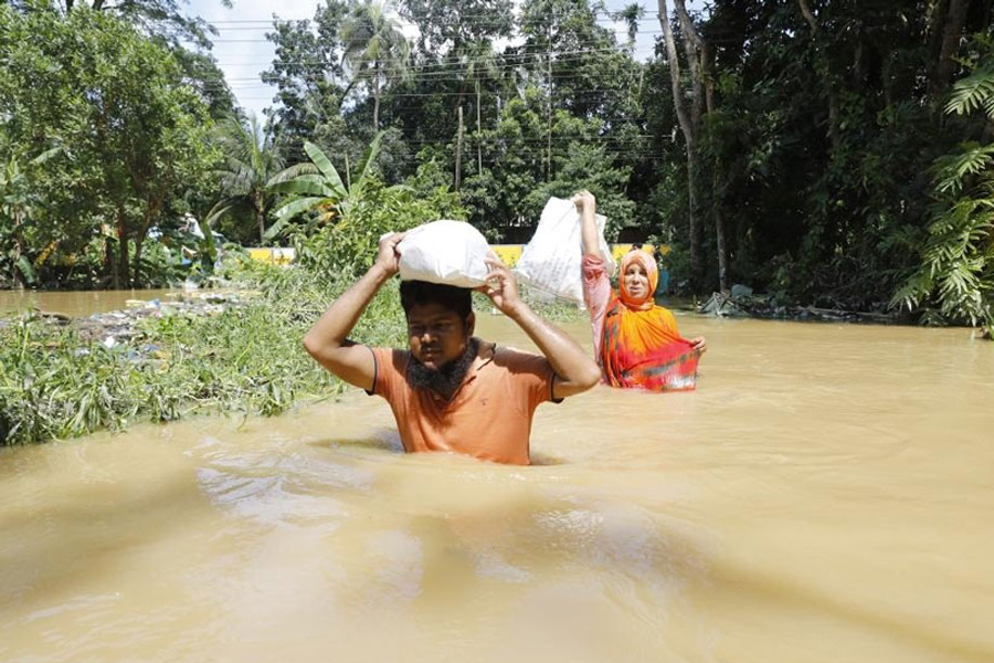 People wade through floodwater on a road in Feni on August 24 — Xinhua photo