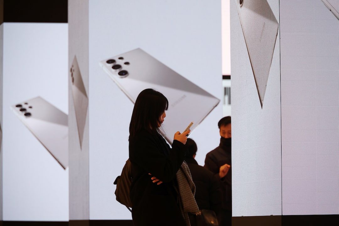 A woman uses her mobile phone in front of electronic boards promoting Samsung Electronics' new flagship smartphones Galaxy S24 series in Seoul, South Korea, January 18, 2024. REUTERS/Kim Hong-Ji/File Photo