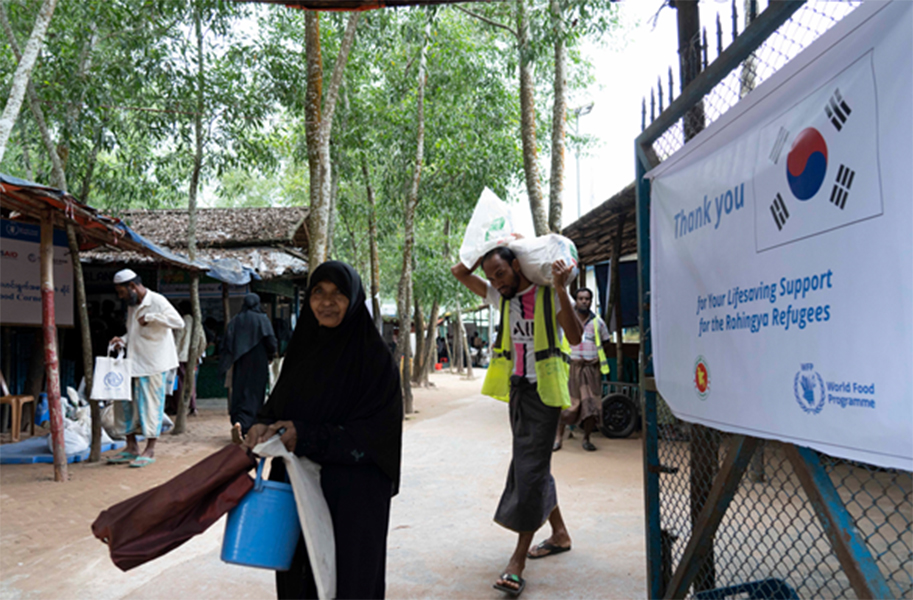 A Rohingya woman leaves a WFP e-voucher outlet after purchasing food for her family in Cox’s Bazar. Since August, all Rohingya in the Cox’s Bazar camps have received their full food assistance, amounting to US$12.50 per person per month. Behind her, a porter hired by WFP helps carry her groceries.