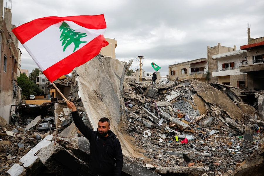 A man waves a Lebanese flag as he stands amidst the rubble of a building destroyed in Israeli strikes, after a ceasefire between Israel and Iran-backed group Hezbollah took effect at 0200 GMT on Wednesday after US President Joe Biden said both sides accepted an agreement brokered by the United States and France, in Tyre, Lebanon, November 27, 2024.