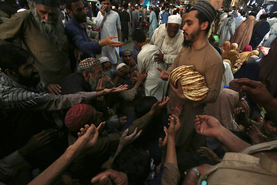 A worker distributes free traditional roti or bread among needy people at a restaurant, in Peshawar, Pakistan, Sunday, April 16, 2023. People are suffering from recent price hike in food, gas, fuel, and power in Pakistan.