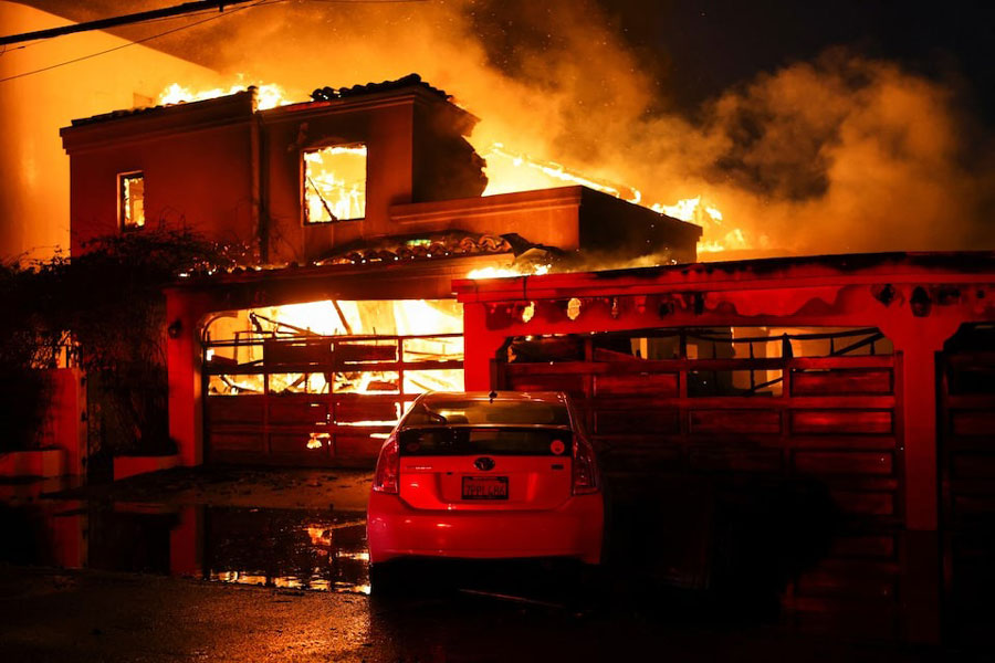 Smoke and flames rise from a burning home, as powerful winds fueling devastating wildfires in the Los Angeles area force people to evacuate, in Malibu, California, US, January 8, 2025.