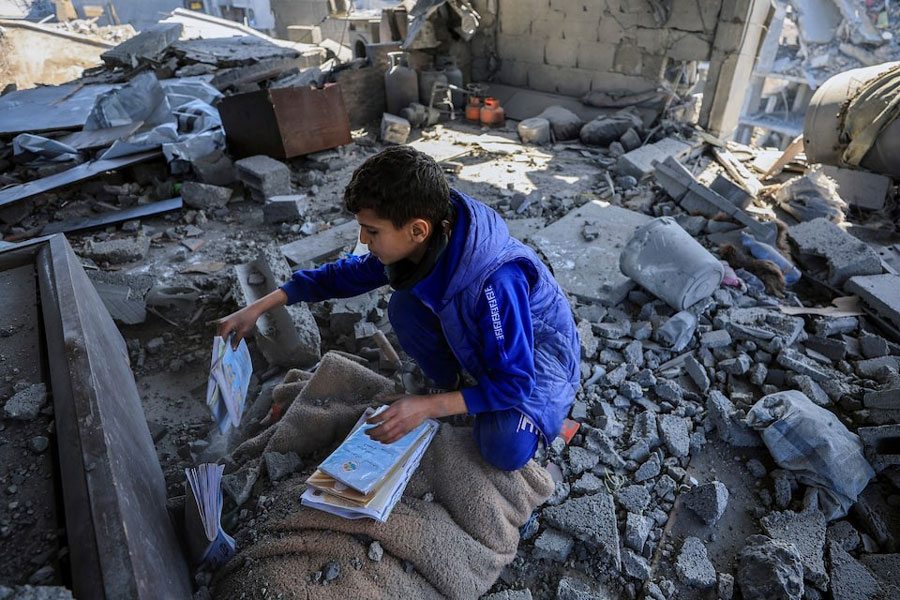A Palestinian boy collects books at the site of an Israeli strike on a house, in Gaza City, March 24, 2025.