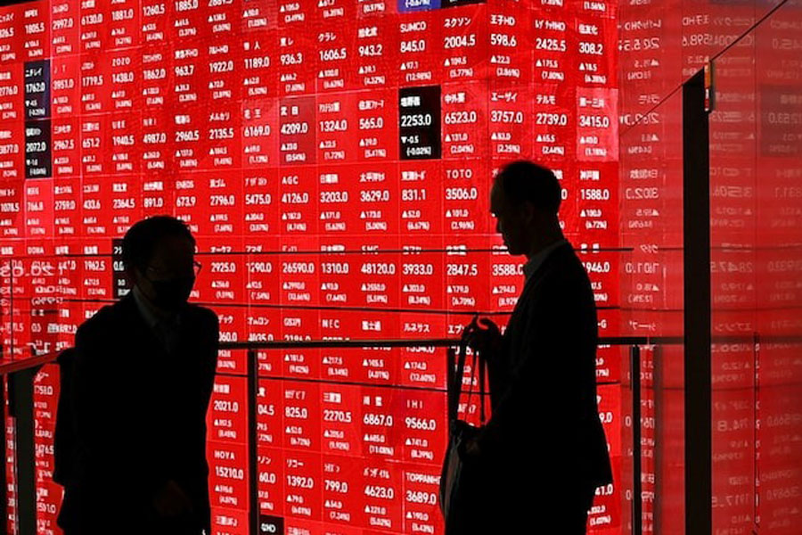 Men stand in front of an electronic stock quotation board inside a builidng in Tokyo, Japan April 8, 2025.