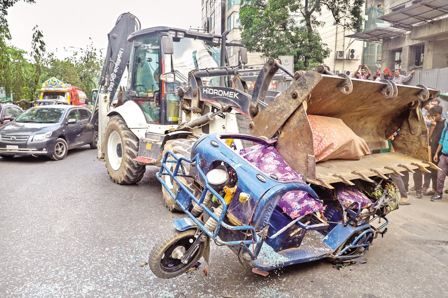 A battery-powered rickshaw is crushed by a bulldozer during a drive against such three-wheelers launched by Dhaka North City Corporation in Dhanmondi area on Tuesday. — FE Photo
