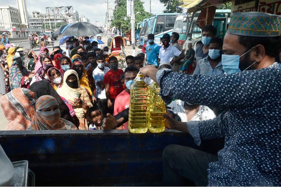 A seller hands two bottles of edible oil to a customer at a government-run fair-price mobile shop in Dhaka, Bangladesh, on July 13, 2021. —Xinhua Photo